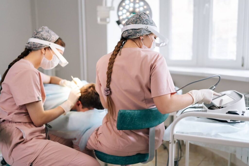 Two trichologist specialists collecting hair follicles from a male patient for hair transplantation in a clinic.