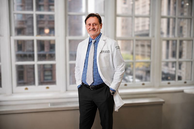 Dr. Cole standing in his office in front of big windows.